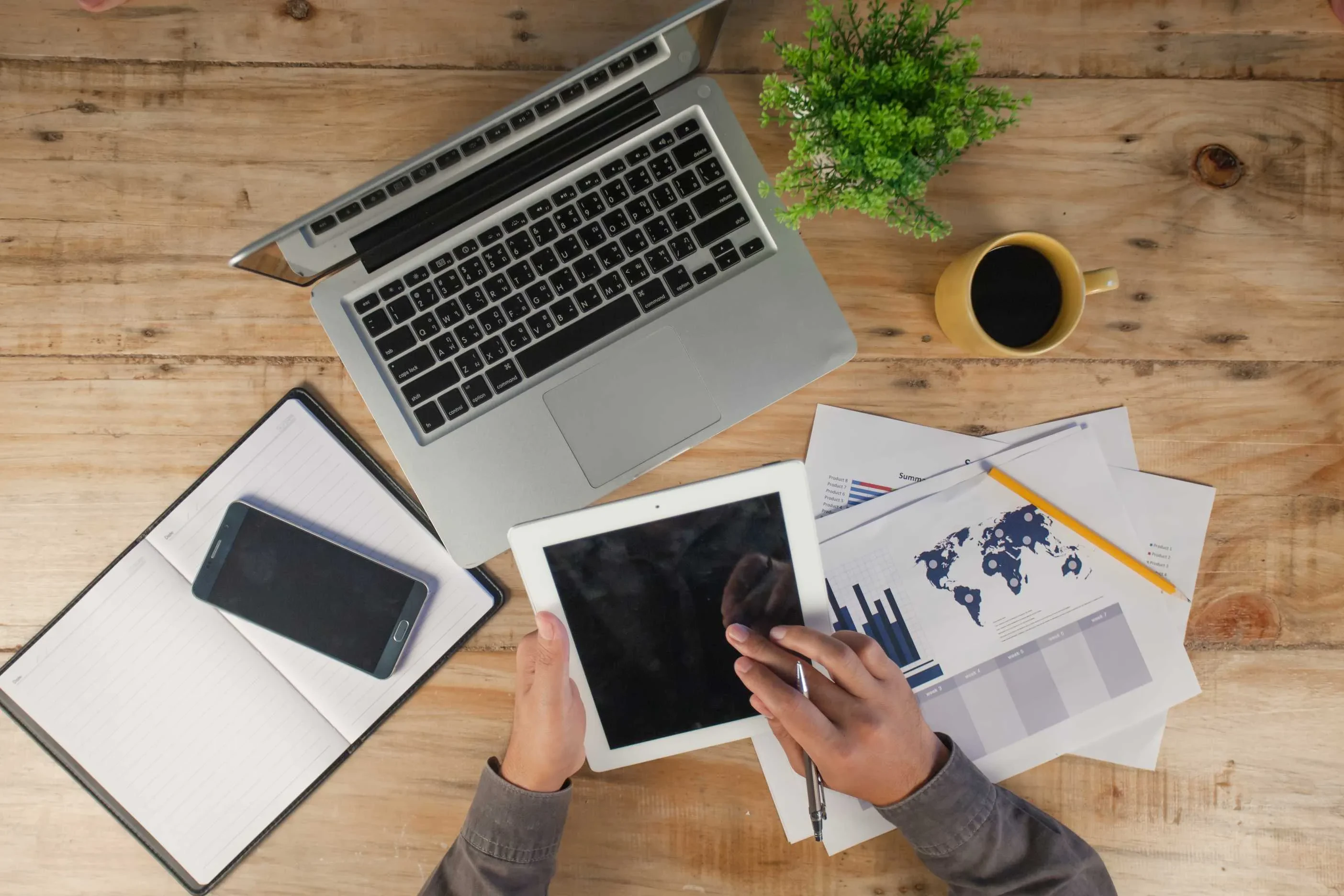 Arbeitsplatz mit Laptop, Tablet, Smartphone und gedruckten Charts – visuelles Motiv für datenbasiertes Projektmanagement und globale Analyseprozesse.