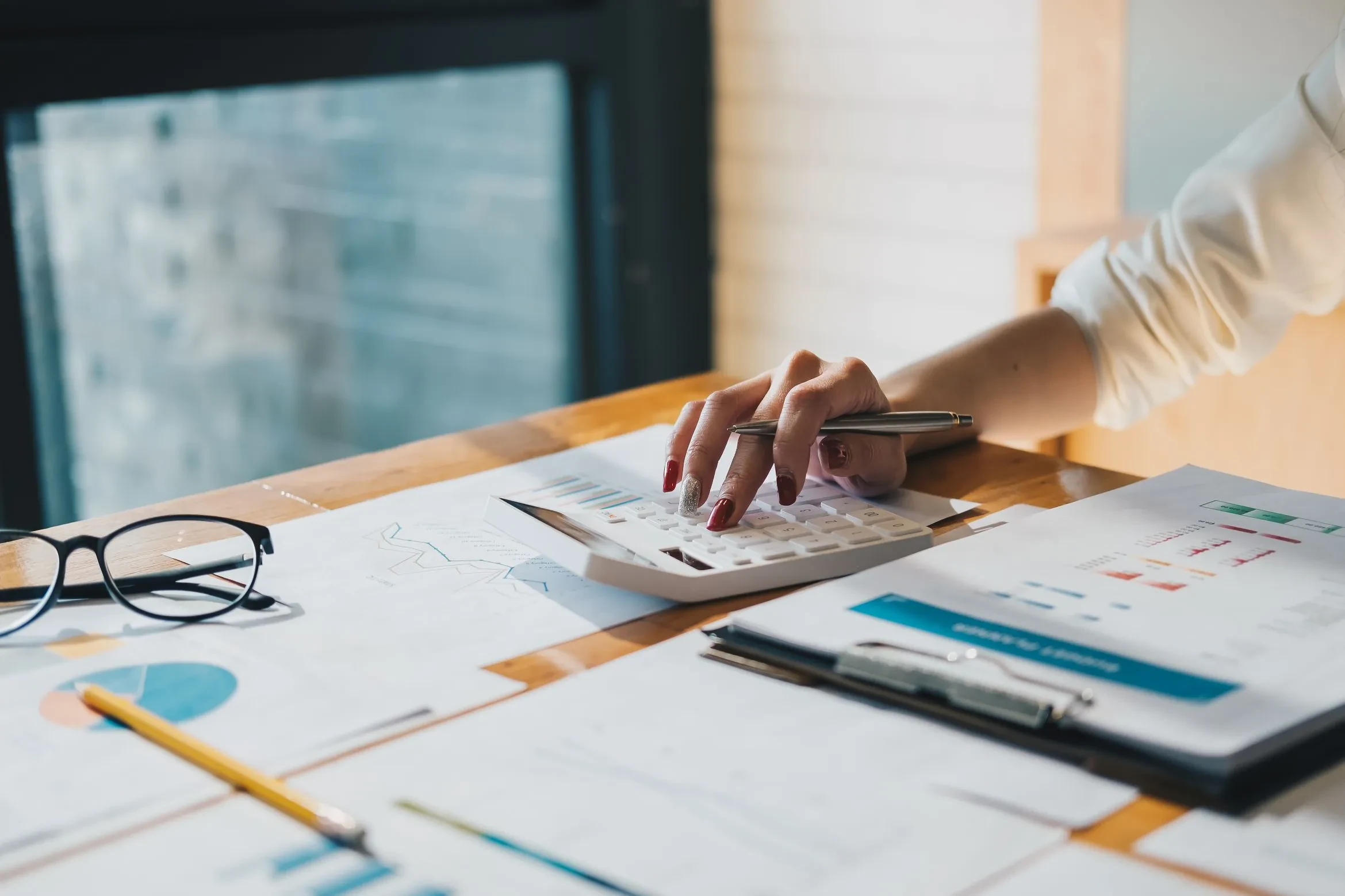 Hand mit Stift auf Taschenrechner über Finanzdokumenten – Symbol für präzises Projektcontrolling und Budgetanalyse