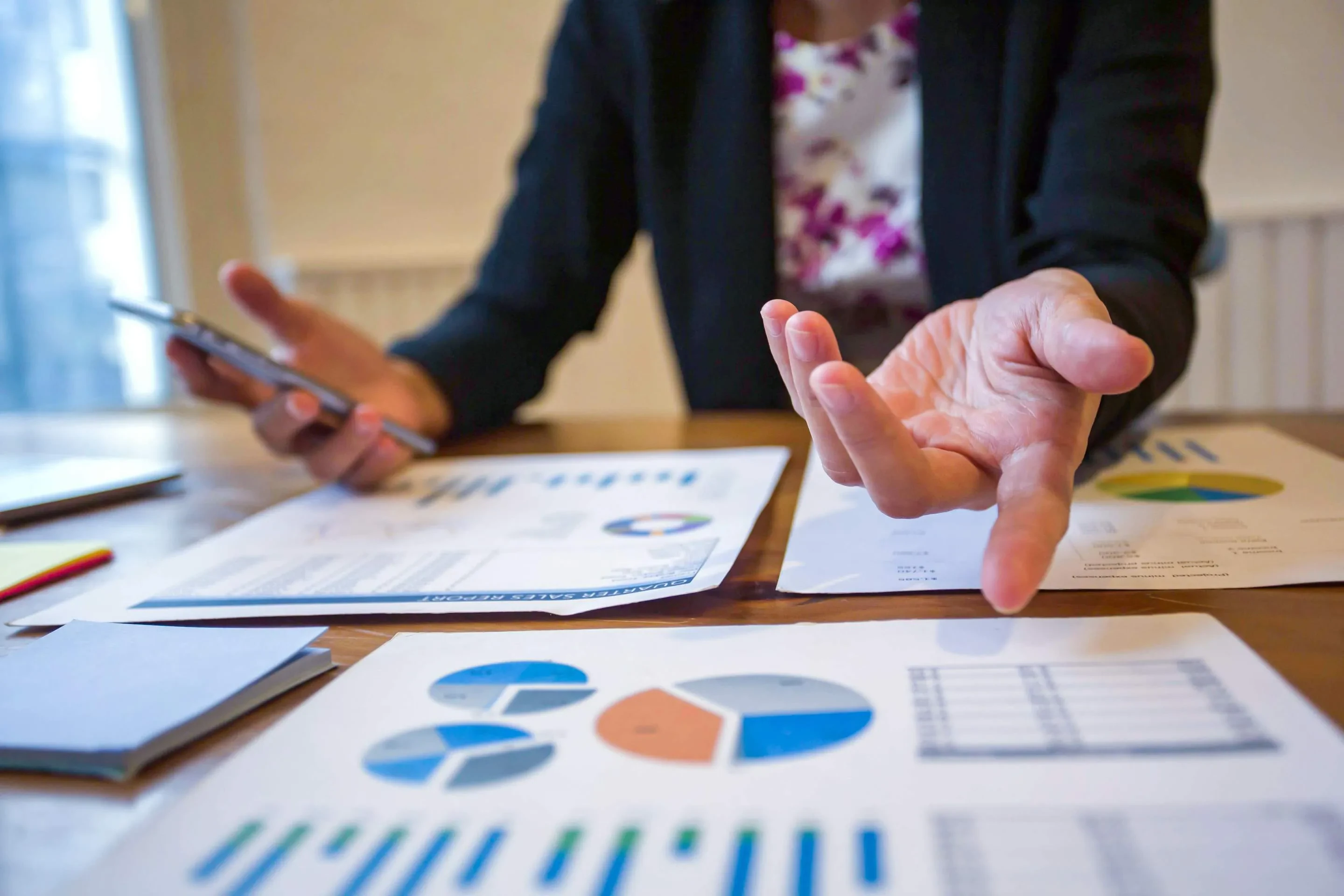 Person mit Smartphone und Charts am Tisch – Symbol für datenbasierte Projektbesprechung und strategische Planung