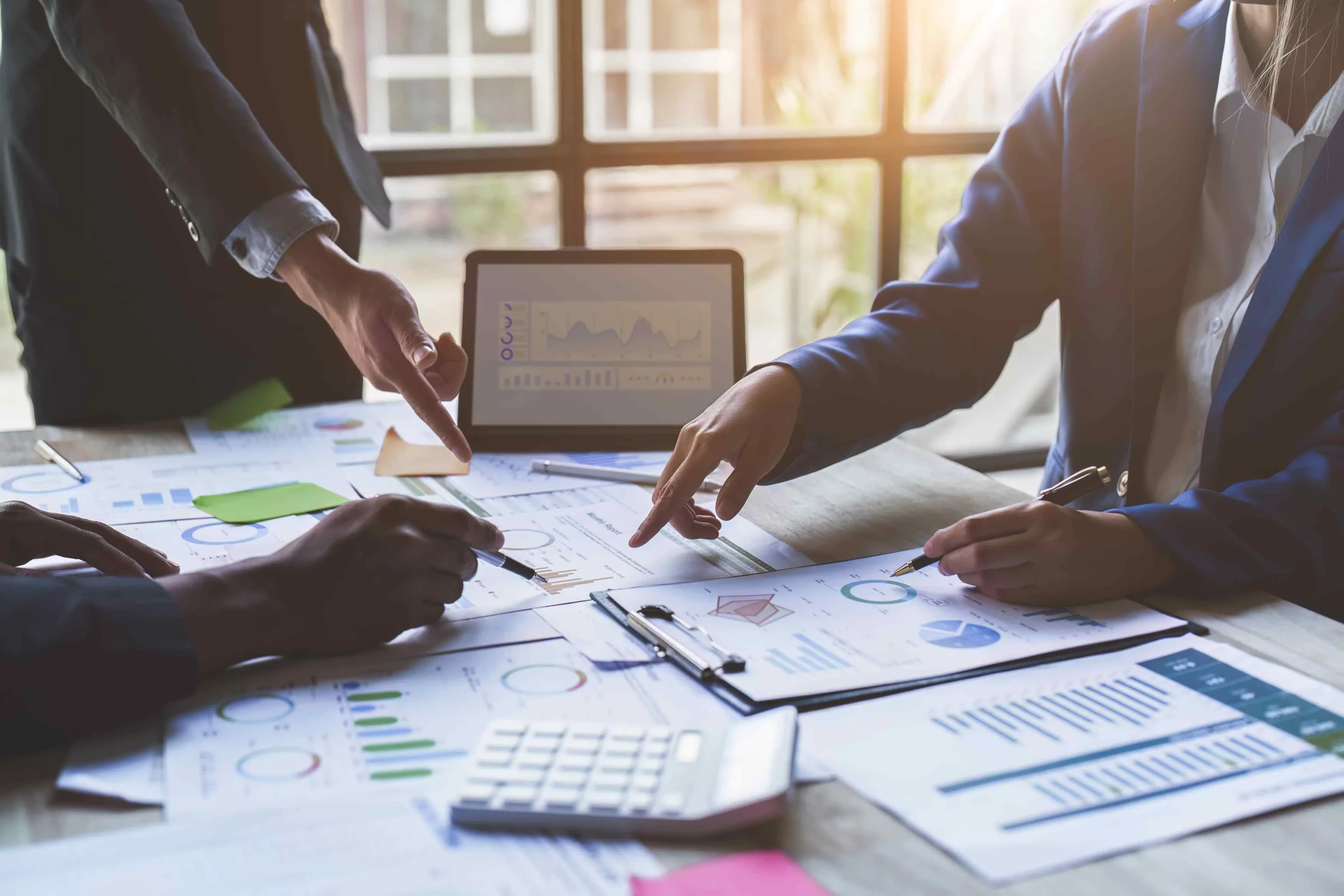 Person zeigt auf Tablet mit Liniendiagramm im Teammeeting – Symbol für datenbasierte Zusammenarbeit und strategische Projektplanung