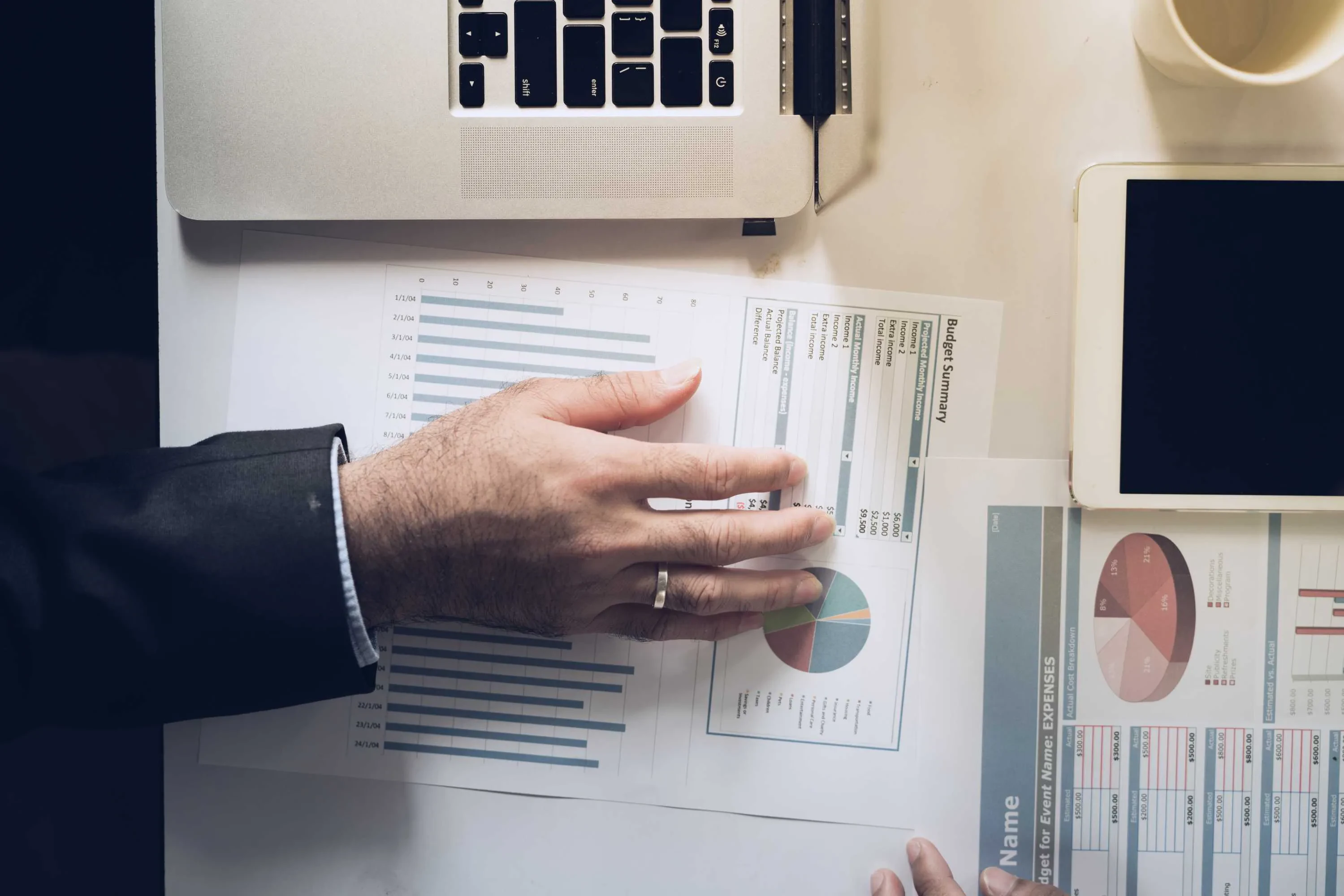 Person zeigt auf Diagramme mit Laptop und Tablet – Symbol für datenbasierte Projektanalyse und hybride Arbeitsweise